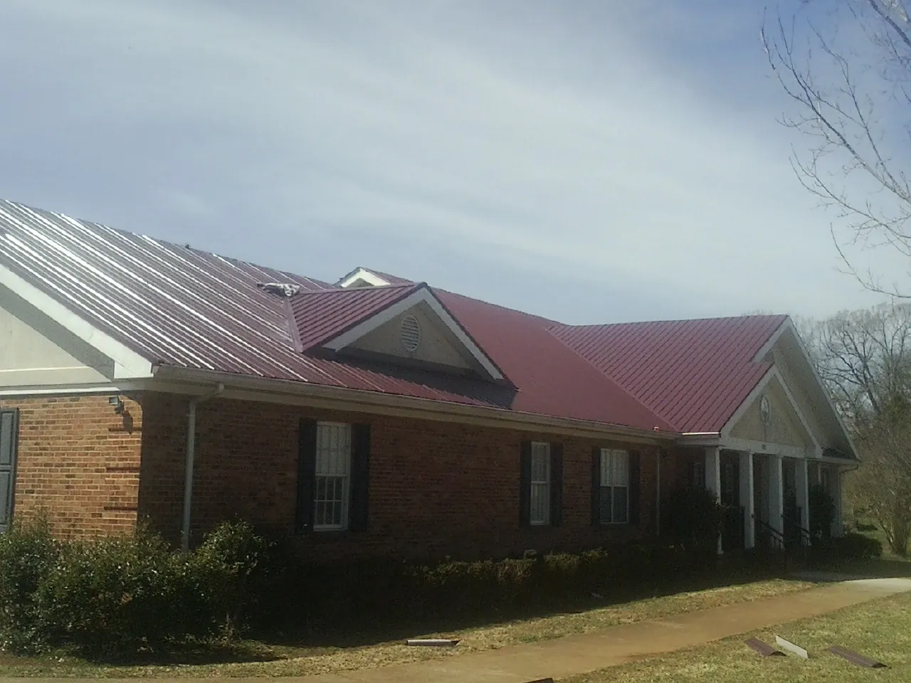 Red metal roof with gabled entries on a long brick building, from a Hail Damage Roof Repair job in Naselle