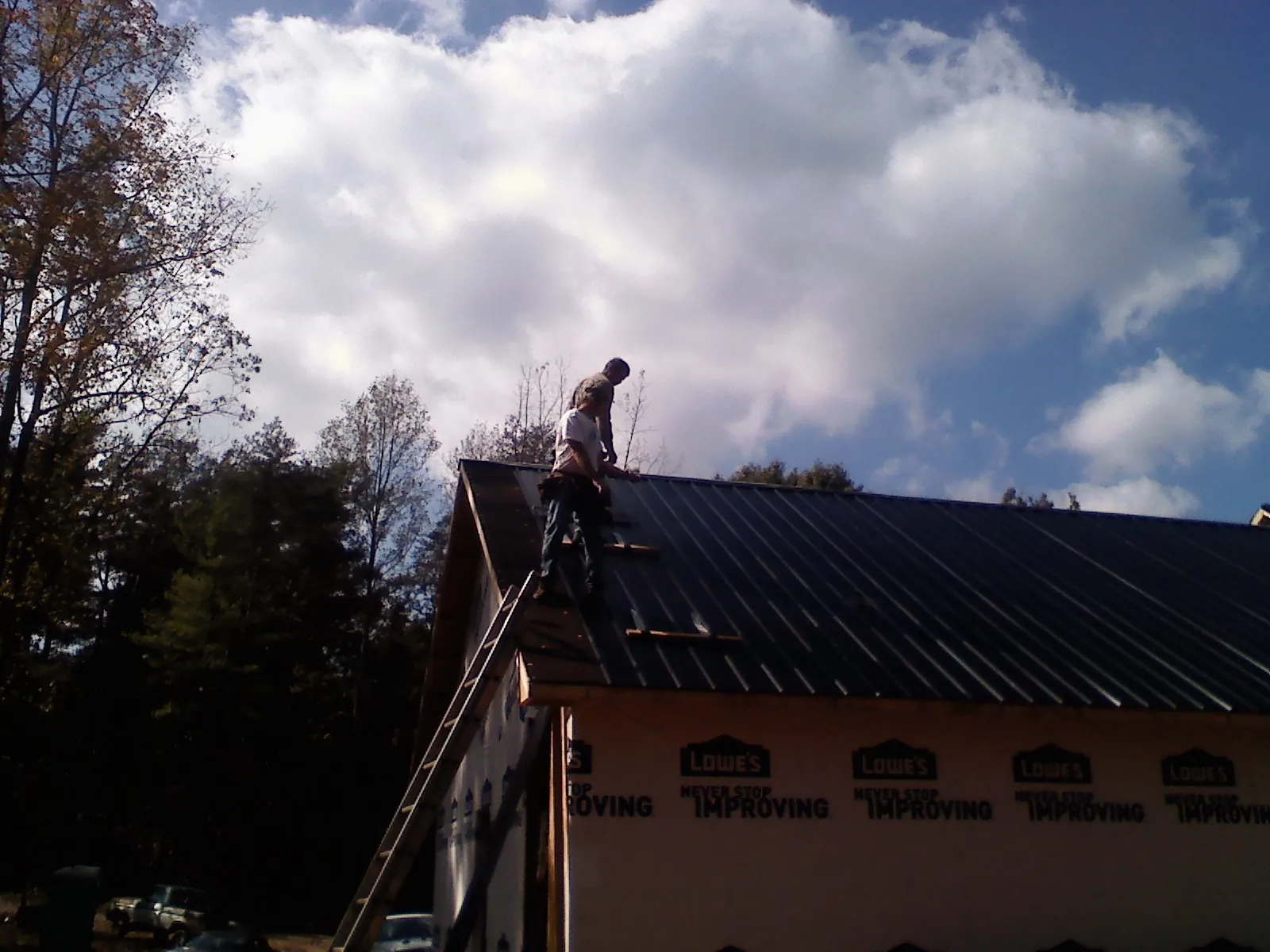 Roofer fastening dark metal panels high against a cloudy sky, from a Roof Inspection job in Naselle