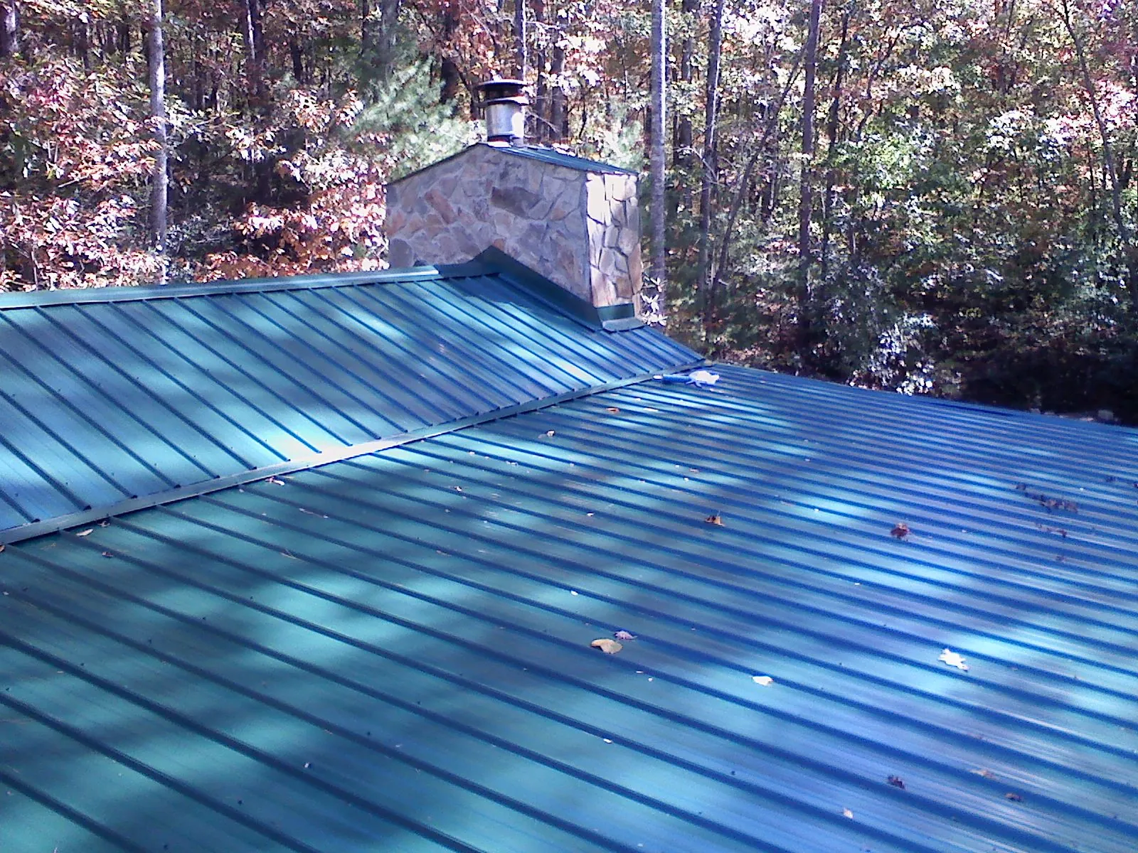 New green metal roof and stone chimney surrounded by autumn woods in Naselle