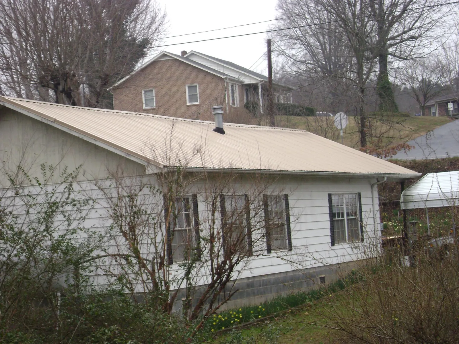 Tan metal roof on a white sided house set into a hillside — Commercial Roofing by Roofing Brothers in Naselle